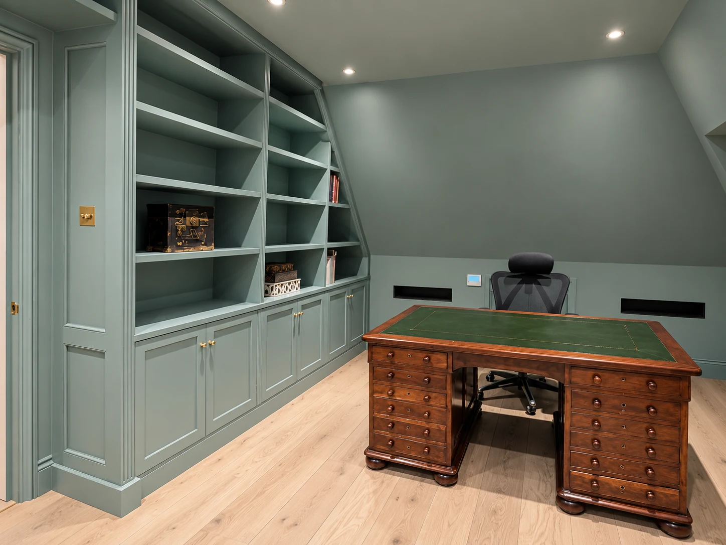 Painted green-grey fitted study cabinetry with open shelving and brass handles